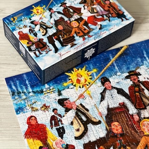 May include: A jigsaw puzzle with a winter scene featuring people in traditional clothing, a sun, and text. The puzzle box is blue with the same image. The puzzle pieces are white with a detailed illustration.