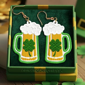 May include: St. Patrick's Day themed earrings shaped like beer mugs with green shamrocks. The earrings are displayed in a green and yellow striped box, with a green leprechaun hat and gold coins in the background. The earrings have gold hooks.