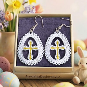 May include: White and gold cross earrings with a decorative oval frame. The earrings are displayed in a gift box with a purple interior, alongside Easter eggs and a small bunny figurine. A vase of flowers is in the background.