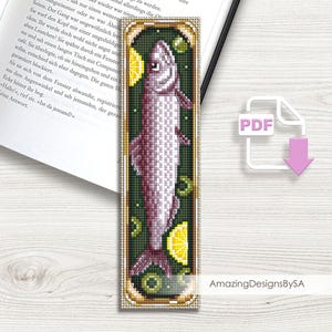 以下が含まれることがあります： レモンとオリーブを添えた缶詰の魚をモチーフにしたブックマークのクロスステッチパターン。パターンは金色の枠で囲まれ、緑色の背景になっています。画像には「PDF」と「Amazing DesignsBySA」のテキストが表示されています。