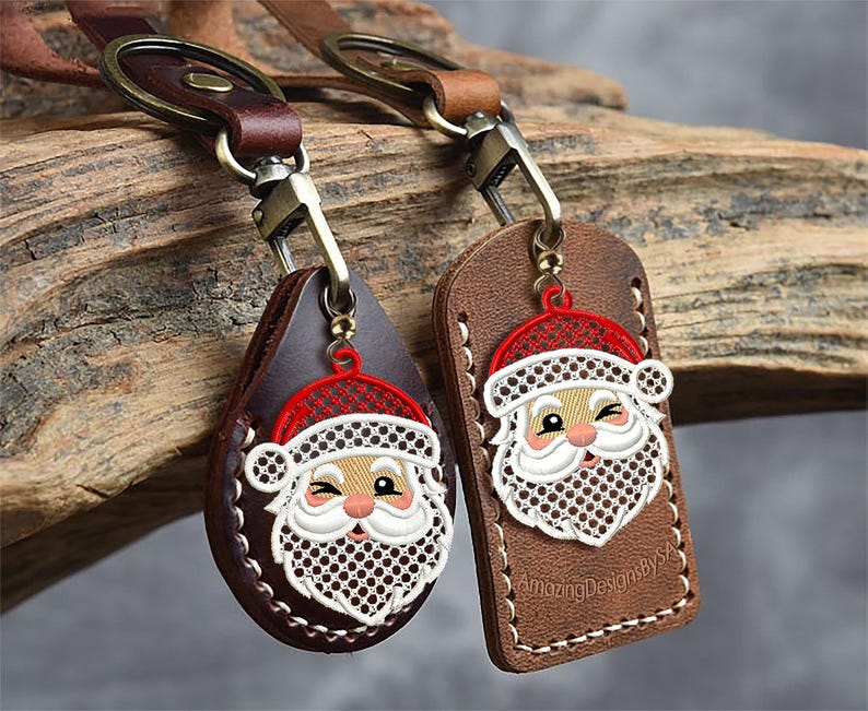 May include: Two leather keychains with Santa Claus designs. One is teardrop-shaped, the other rectangular. Both have a red hat, white beard, and a winking face. The keychains are brown with metal hardware and stitched edges.