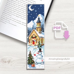 May include: A cross-stitch bookmark featuring a winter scene. The design includes a church, snowman, Christmas tree, and falling snow under a starry night sky. The bookmark has the text "Amazing DesignsBySA".