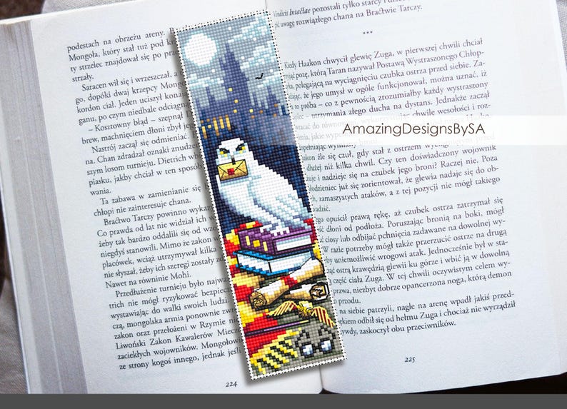 May include: A white owl with a letter in its beak perched on a stack of books. The owl is in front of a dark blue background with a castle in the distance. The bookmark is made of cross-stitch.