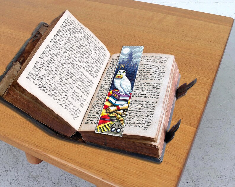 May include: A bookmark featuring a white owl perched on a stack of books with a Hogwarts castle background. The bookmark is made of fabric and has a colorful design.