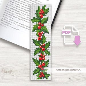 May include: A white cross-stitch bookmark featuring a repeating pattern of green holly leaves and red berries. The bookmark is rectangular and has the text "AmazingDesignsBySA" on the bottom right.