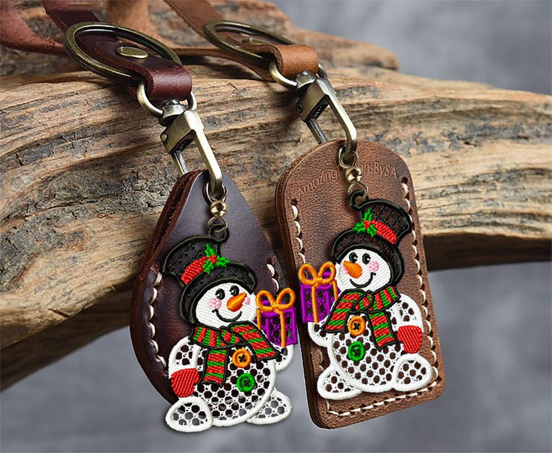 May include: Two leather keychains with a snowman design. The snowmen have black top hats, orange carrot noses, and red mittens. One keychain is teardrop-shaped, the other is rectangular. Both have a metal clasp and a brown leather strap.