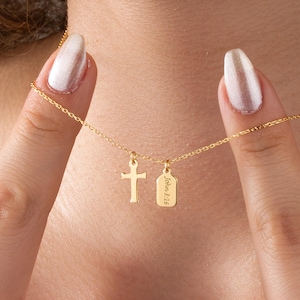 May include: A gold-colored necklace featuring a small cross pendant and a rectangular tag pendant. The tag is engraved with the text "John 3:16". The necklace is displayed against a skin-toned background.