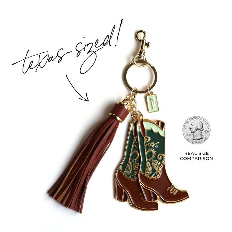 May include: A gold-tone keychain with a brown leather tassel and a charm of two green and gold cowboy boots. The boots are about the size of a US quarter, as shown in the image. The keychain also has a gold-tone ring and a lobster clasp.