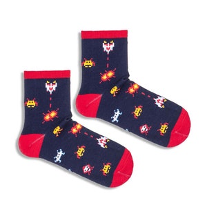 May include: A pair of navy blue socks with red cuffs and toes. The socks are patterned with pixelated retro video game graphics in white, yellow, and red. The design includes spaceships and explosions.