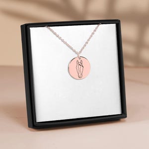 Puede incluir: Un collar de cadena de plata con un colgante redondo que presenta un dibujo lineal de la cabeza de un caballo. El colgante es de color oro rosa.