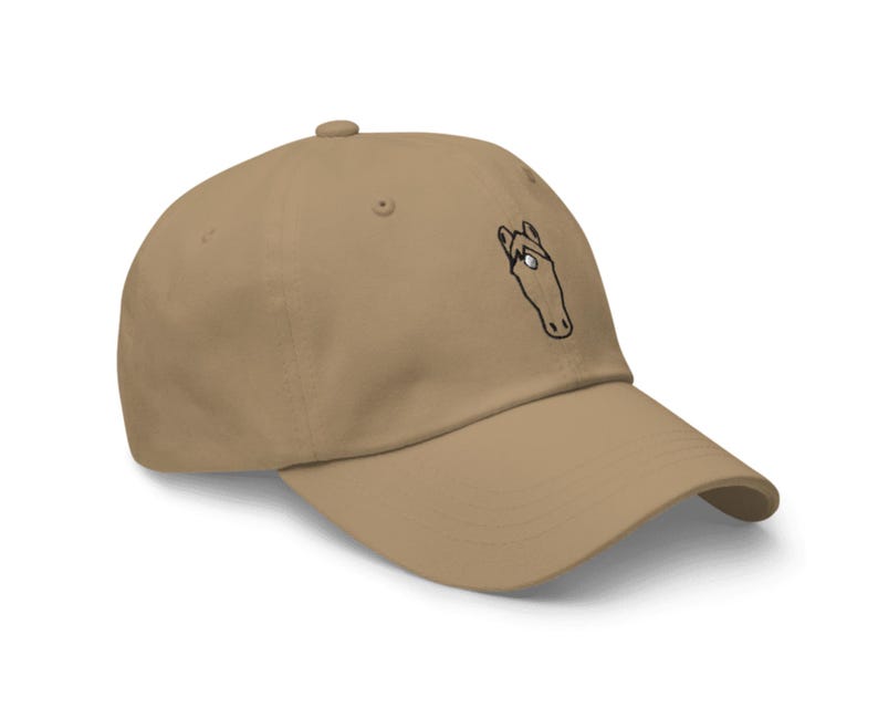May include: A tan baseball cap with a black and white horse head design embroidered on the front.