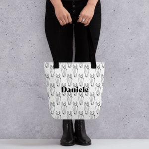 May include: White tote bag with a black and white horse head pattern and the name "Daniele" printed in black.