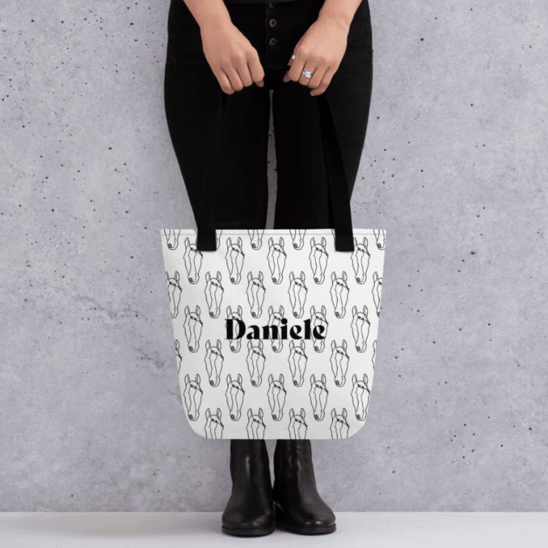 May include: White tote bag with a black and white horse head pattern and the name "Daniele" printed in black.