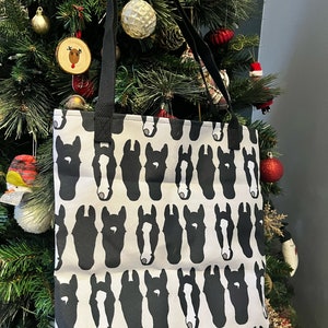 May include: A white tote bag with a black and white horse head pattern. The bag has black straps.