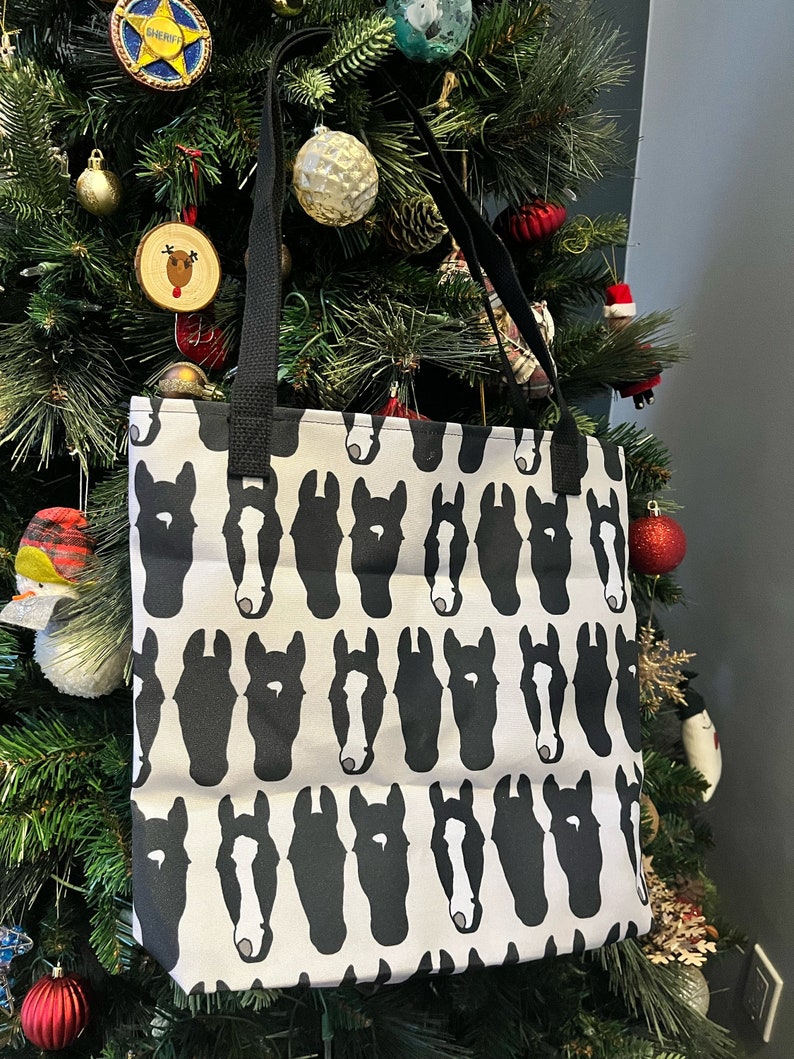 May include: A white tote bag with a black and white horse head pattern. The bag has black straps.