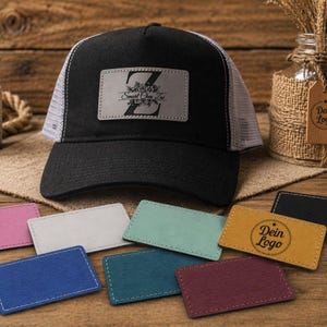 Könnte beinhalten: Schwarze Trucker-Kappe mit weißem Mesh-Rücken und einem grauen Lederpatch. Der Patch zeigt einen stilisierten Buchstaben "Z" mit floralen Akzenten und dem Text "Smart Once Lee". Mehrere farbige Lederpatches werden angezeigt.