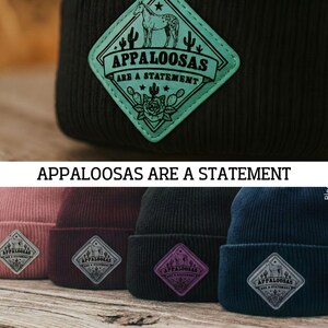 Puede incluir: Gorro de punto acanalado negro con un parche turquesa con una ilustración de un caballo, cactus y el texto "APPALOOSAS ARE A STATEMENT". También se ven otros gorros en rosa, burdeos, negro y azul marino.