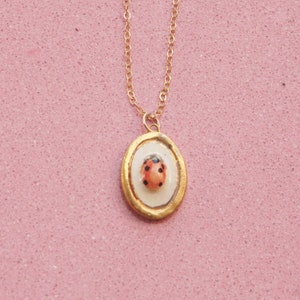 Peut inclure: Un collier en chaîne dorée avec un pendentif représentant une coccinelle rouge dans un cadre ovale doré.