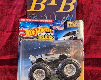 May include: A Hot Wheels Monster Trucks toy featuring a silver DeLorean Time Machine. The packaging includes the text "BACK TO THE FUTURE - TIME MACHINE" and "Hot Wheels Monster Trucks". The toy has large black wheels and is suitable for ages 3+.