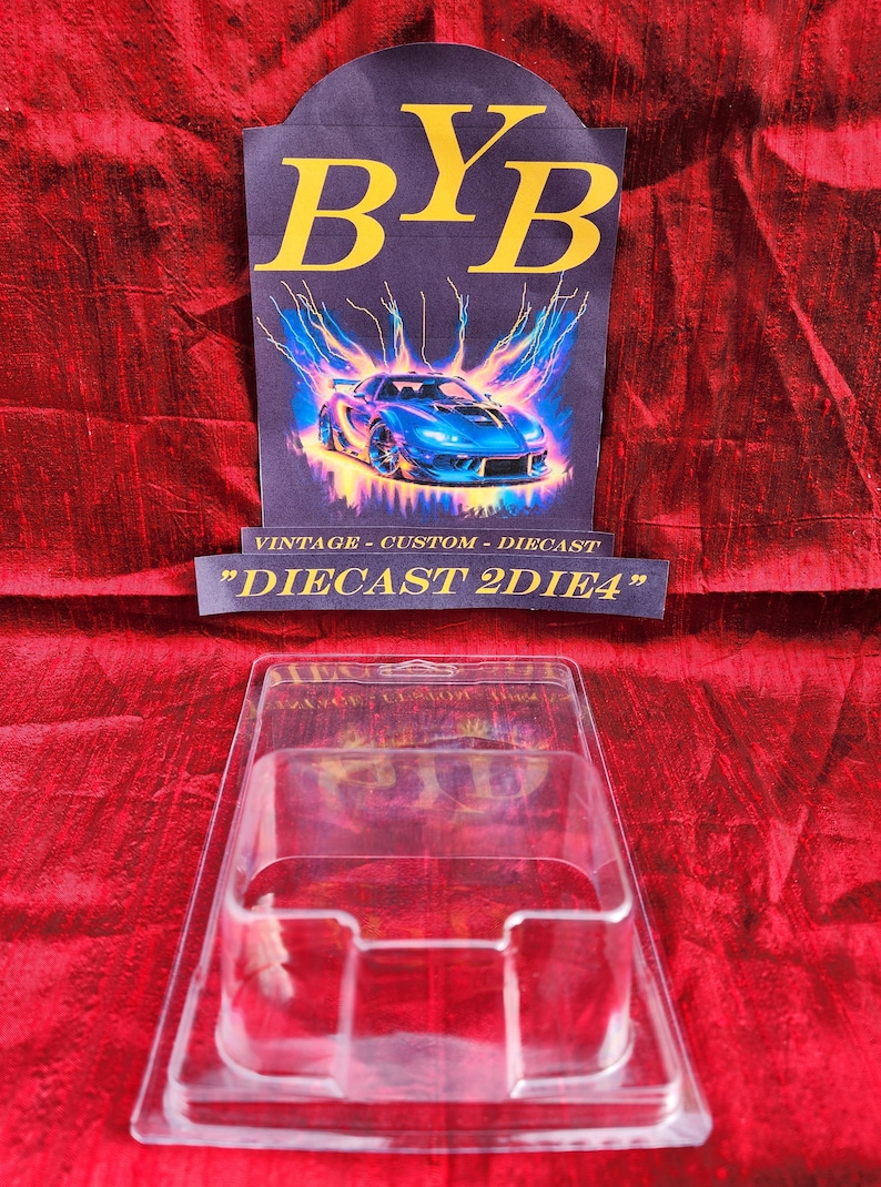 May include: A clear plastic diecast car display case sits in front of a sign with the text "BYB" in yellow letters. The sign also features a blue sports car graphic with lightning bolts and the text "VINTAGE - CUSTOM - DIECAST" and "DIECAST 2DIE4".