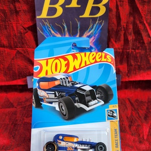 May include: A Hot Wheels Mod Rod die-cast toy car in a blue and orange color scheme. The car is on a blue and white card with the Hot Wheels logo. The card also has the text "HW 55 RACE TEAM" and "MOD ROD".