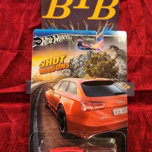 May include: Red Hot Wheels diecast toy car model of an Audi RS6 Avant wagon. The car has black accents and a black spoiler. The car is on a white background with a blue and orange sky. The packaging has the Hot Wheels logo and the words "Hot Wagons".