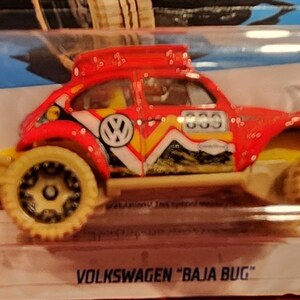 May include: A red Volkswagen Baja Bug toy car with a white and yellow racing stripe, a black VW logo, and the number "633" on the side. The car has a tan roof rack and tan off-road tyres.