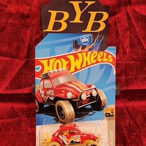 May include: A red Hot Wheels Baja Blazers die-cast toy car with a white and yellow stripe design. The car has a black grill, black headlights, and a black VW logo. The car is on a blue background with the words "Hot Wheels" in white letters. The car is numbered 241/250 and 9/10.
