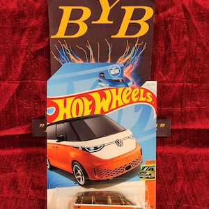 May include: Orange and white Volkswagen ID. Buzz Hot Wheels toy car in a blue and white package. The package has the Hot Wheels logo and the text "2022/250" and "2/5".