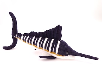 May include: A crocheted marlin fish toy with a blue, white, and gold striped pattern. The marlin has a long, pointed snout and a dorsal fin.