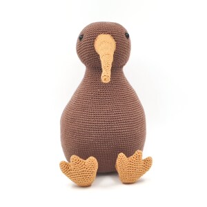 May include: A brown crocheted kiwi bird plush toy with orange feet. The toy has black eyes and a long orange beak.