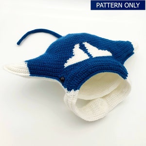 May include: A crocheted manta ray hat in blue and white. The hat has a long tail and a white crocheted brim.