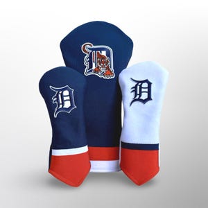 Puede incluir: Tres fundas para la cabeza del palo de golf en azul marino, blanco y rojo. Las fundas azul marino presentan un logotipo "D" blanco, y la funda central tiene un logotipo de tigre. Las fundas tienen una base roja.