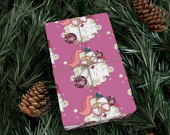 Puede incluir: Un regalo envuelto con un patrón de Papá Noel rosa, atado con hilo, descansa sobre un lecho de agujas de pino y piñas. El diseño de Papá Noel presenta gafas de sol, una bola de discoteca y margaritas.