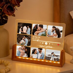 May include: A personalized photo display with a wooden base and a clear acrylic panel featuring multiple photos. The panel includes the text "All My Life KC and Joe" and "Sophia Jackson" with music-themed icons and a heart.