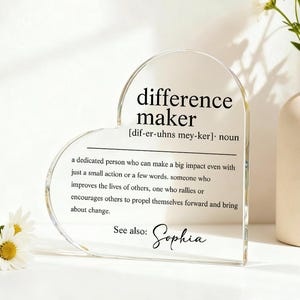 May include: Clear acrylic heart-shaped plaque with the definition of "difference maker" printed in black. The definition includes the pronunciation and a description of the term. The name "Sophia" is also included.