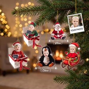 May include: Five hanging Christmas ornaments featuring photos of children in holiday costumes. Designs include babies in gift boxes, a child in a penguin suit, a child in a Santa suit, a child in a sleigh, and a blank photo frame labelled YOUR PHOTO.