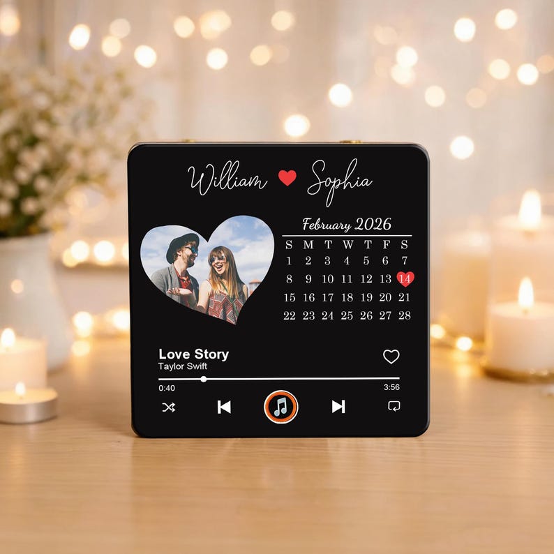 May include: A black, square music plaque with a heart-shaped photo. It displays the names "William" and "Sophia", a February 2026 calendar, and the song "Love Story" by Taylor Swift. The plaque has music player controls.