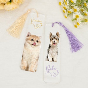 May include: Two personalized glass bookmarks with a cat and a dog on them. The cat bookmark has a cream tassel and the text "Vivian" with a heart and paw prints. The dog bookmark has a purple tassel and the text "Bella" with a heart and paw prints.
