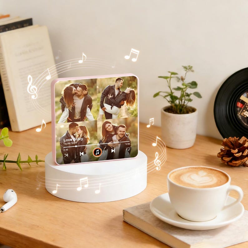 May include: A pink square photo frame with four images of a couple, surrounded by musical notes. The frame is on a white stand, beside a coffee cup and a small plant. The photos depict a couple in romantic poses. The frame is a modern home decor item.