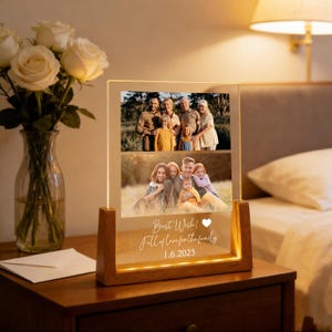 May include: A wooden-based illuminated photo display featuring two family photographs. The clear acrylic front displays the text "Best Wish! Full of love for the family 1.6.2025". The display is lit from within, creating a warm glow.