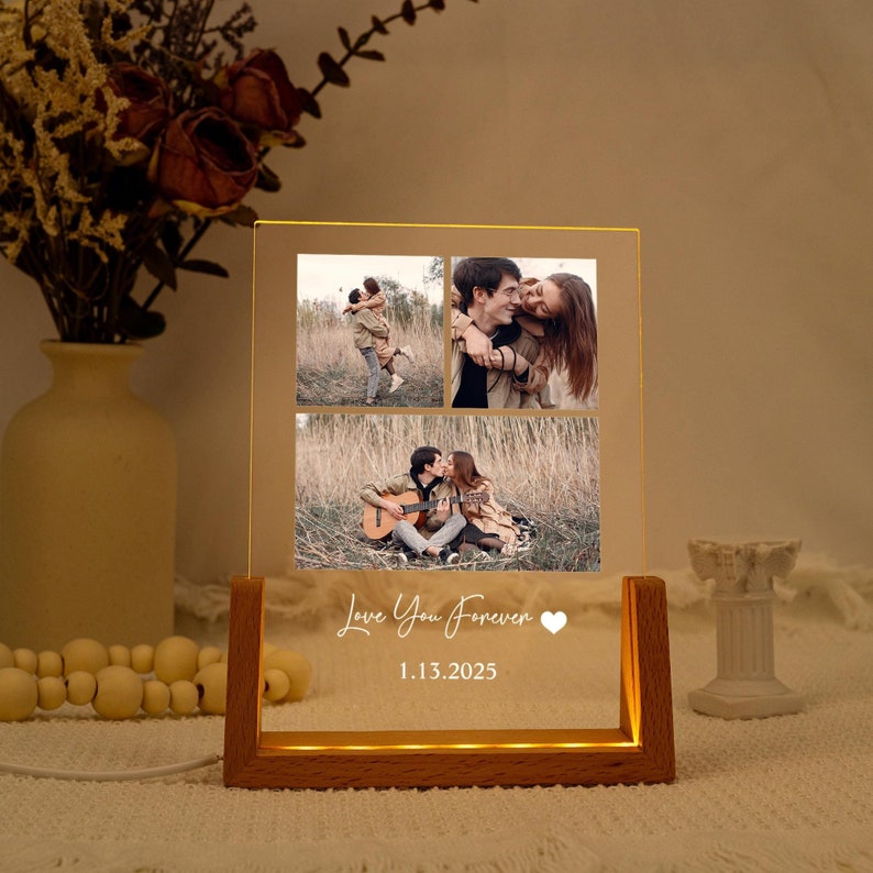 May include: A wooden-based, illuminated acrylic photo display. It features three photographs of a couple and the text "Love You Forever" with a heart symbol and the date 1.13.2025. The display emits a warm, inviting light.