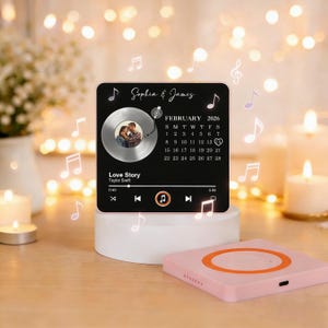 May include: A black square plaque with a photo, a record player graphic, and the text "Sophia & James" and "Love Story". The plaque also features a calendar for February 2026 and musical notes.