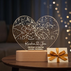 May include: A heart-shaped, illuminated night light with a constellation design. The light is engraved with the names "Keisha & Joe", the date "9.26.2026", and the word "WATERMILL". It sits on a wooden base, with a gift card tied with a gold ribbon.