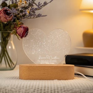 May include: A heart-shaped night light with a constellation design. The clear acrylic heart sits on a wooden base. The text on the light reads "Lewis & Caitlin, The start of our adventure, 29.11.2024, York."