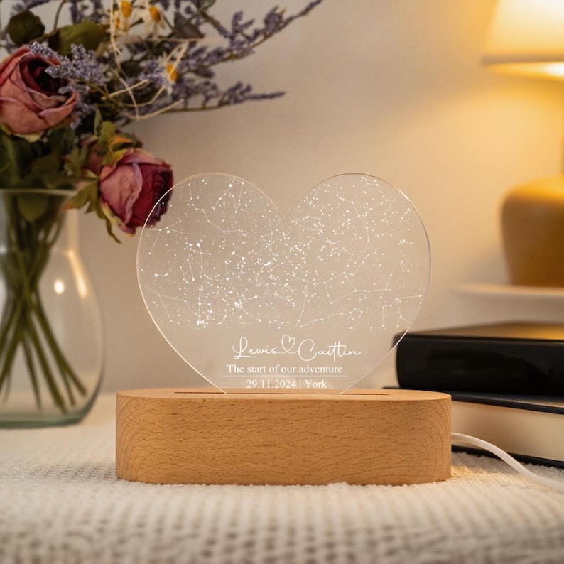 May include: A heart-shaped night light with a constellation design. The clear acrylic heart sits on a wooden base. The text on the light reads "Lewis & Caitlin, The start of our adventure, 29.11.2024, York."