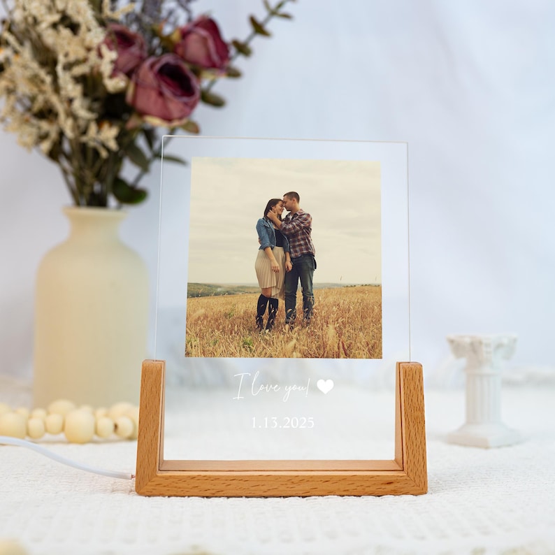 May include: A clear acrylic photo frame with a wooden base, showing a couple in a field. The text "I love you!" and the date 1.13.2023 are printed on the frame. A vase of flowers is in the background.
