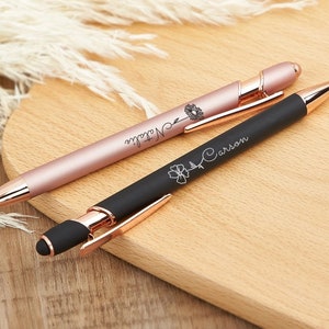 May include: Two personalized pens with rose gold accents. One pen is black with the name "Carson" engraved on it, and the other is pink with the name "Natalie" engraved on it.
