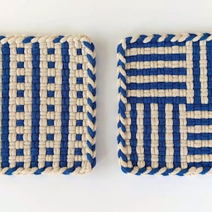 May include: Two square potholders made of woven cotton cord in a blue and cream color scheme. The left potholder features vertical stripes, while the right potholder displays a four-quadrant pattern with alternating horizontal and vertical stripes.
