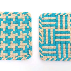 以下が含まれることがあります： ティール色とベージュ色の織りコットンコードで作られた2つの正方形の鍋敷き。左側の鍋敷きは千鳥格子のような繰り返し模様で、右側の鍋敷きは幾何学的なブロックデザインが特徴です。どちらにも小さなループが付いています。